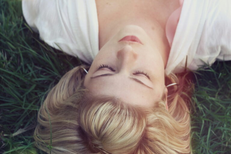 Femme couchée dans l'herbe verte, les yeux fermés, qui se repose au soleil